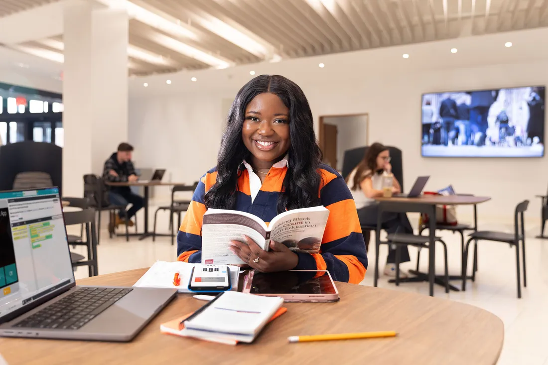 Student reading a book and smiling at the camera