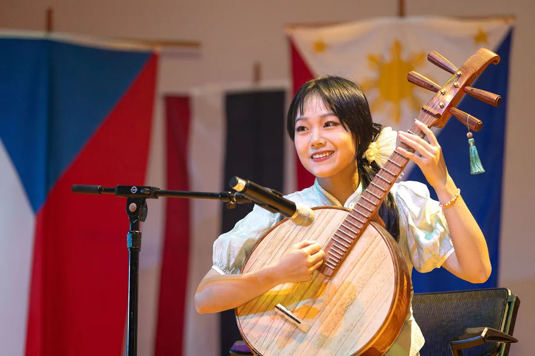 Student stands on stage at talent show with international flags in backdrop.