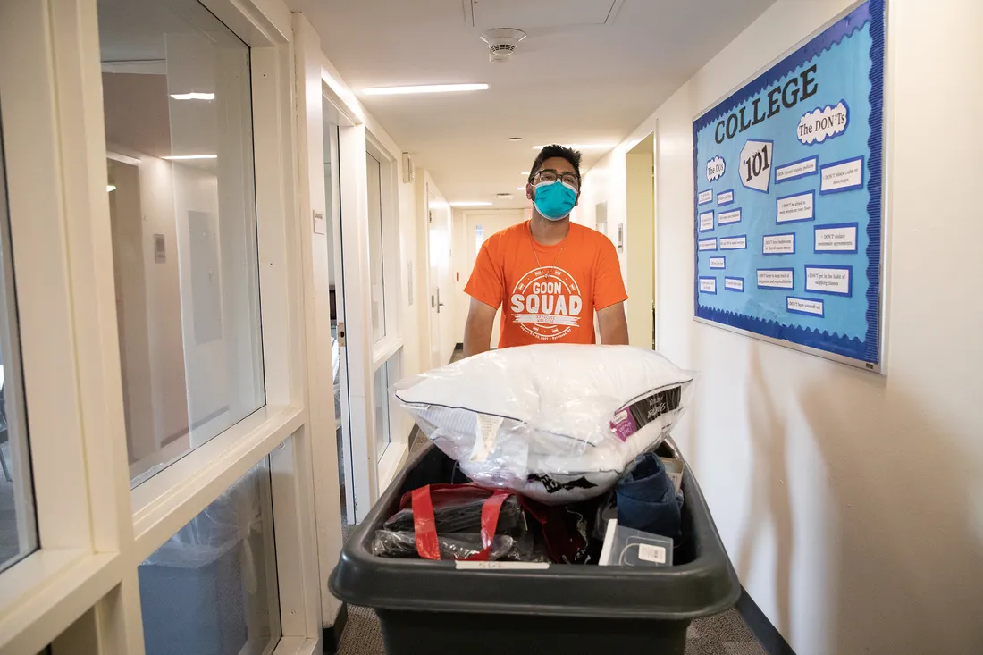 A student pushes a bin full of belongings down a hallway.