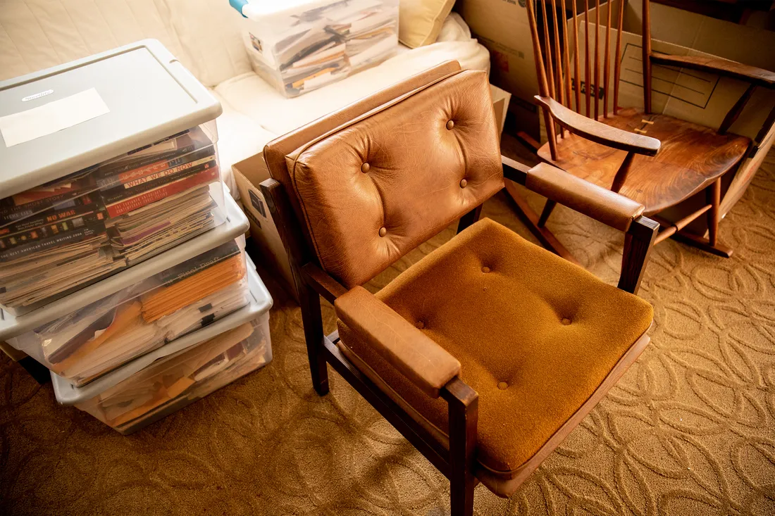 Close-up photo of a worn, leather chair surrounded by boxes of books.