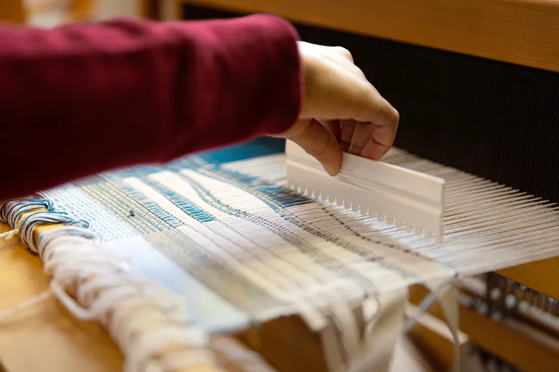 Close up shot of a student weaving a textile design on a loom.