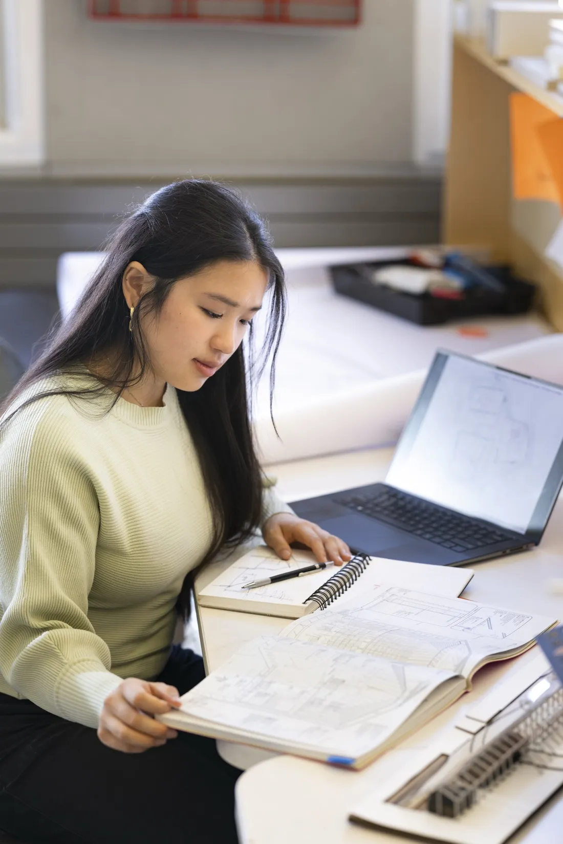 Kate Tang '27 sitting at a desk and looking over architectural sketches.