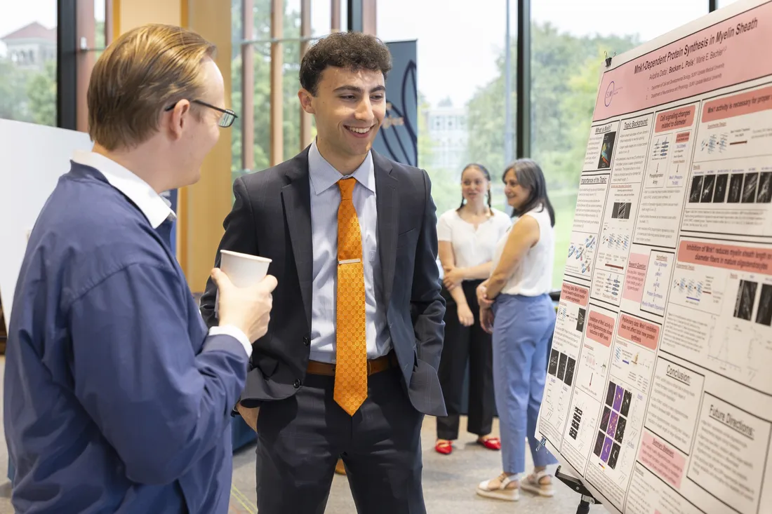 Beckam Polis speaks with another person about his research at The Summit Showcase.