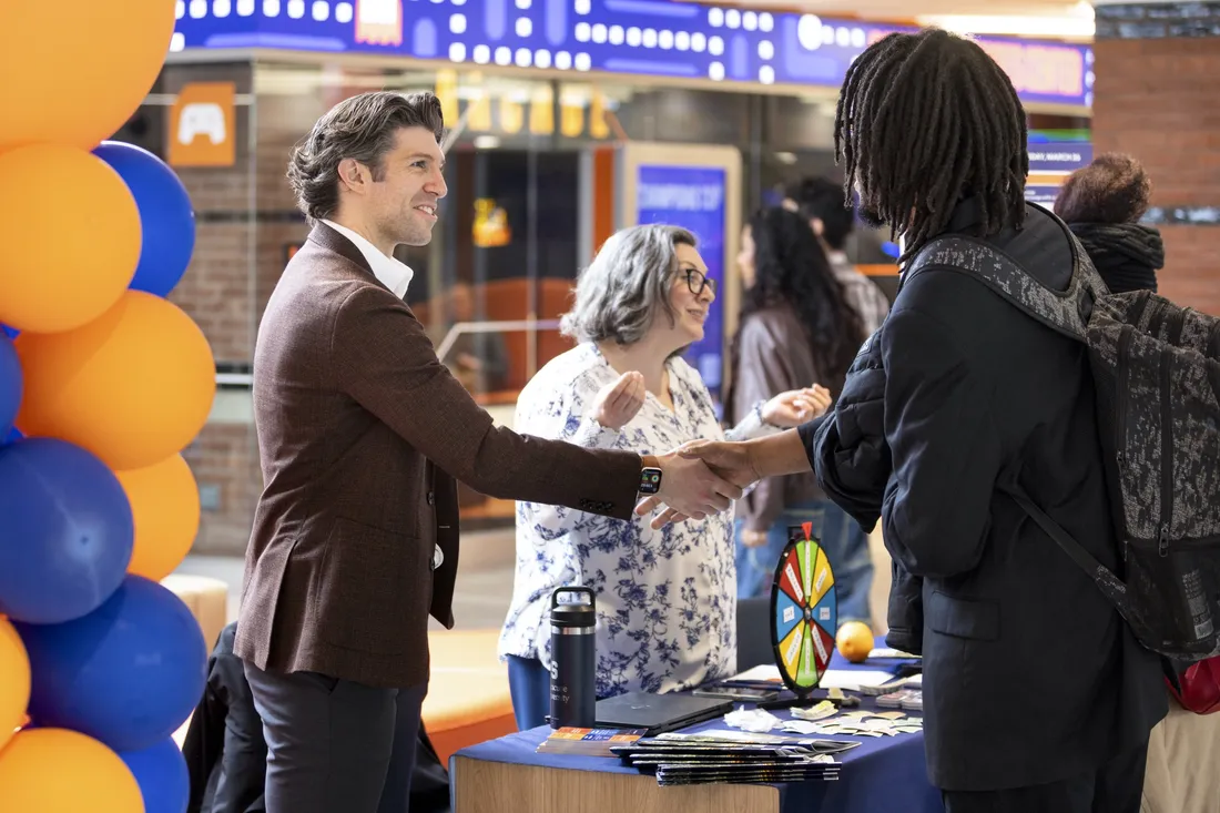 Student at Syracuse University's first Career Conference shaking hands and speaking with an industry professional.