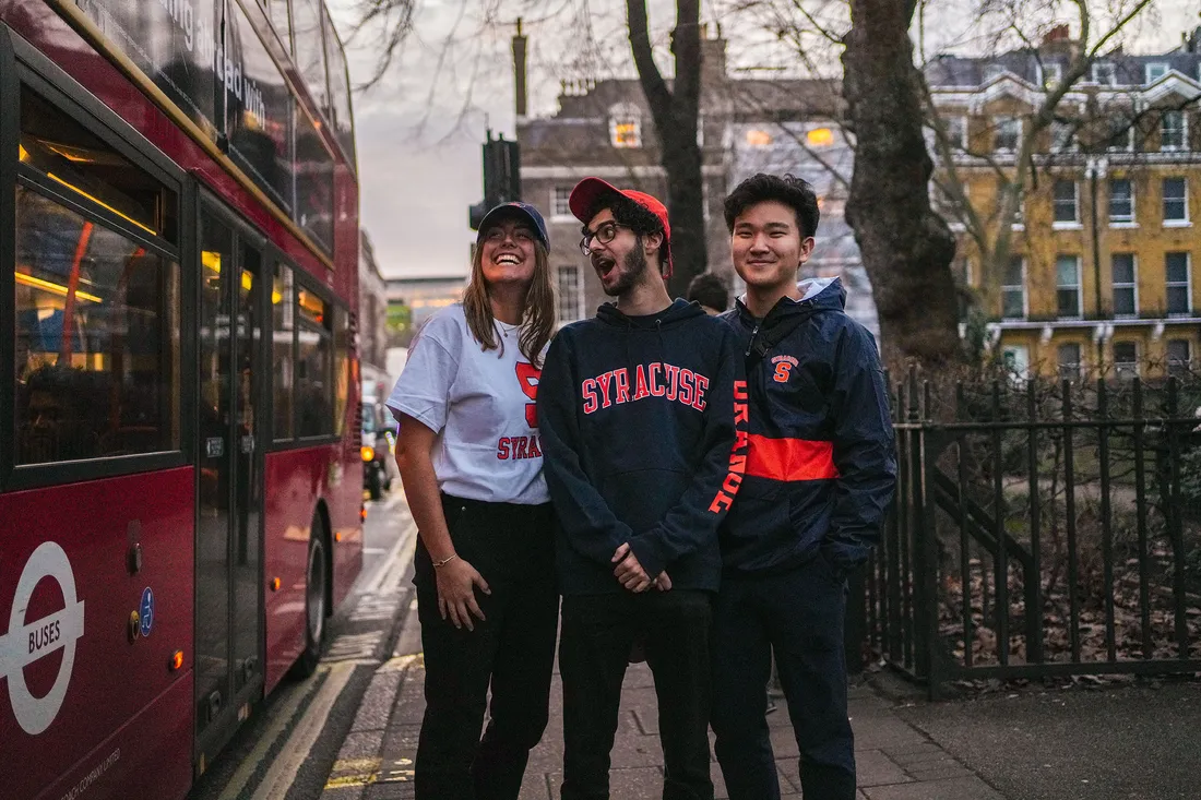 Students pose in front of double decker bus.