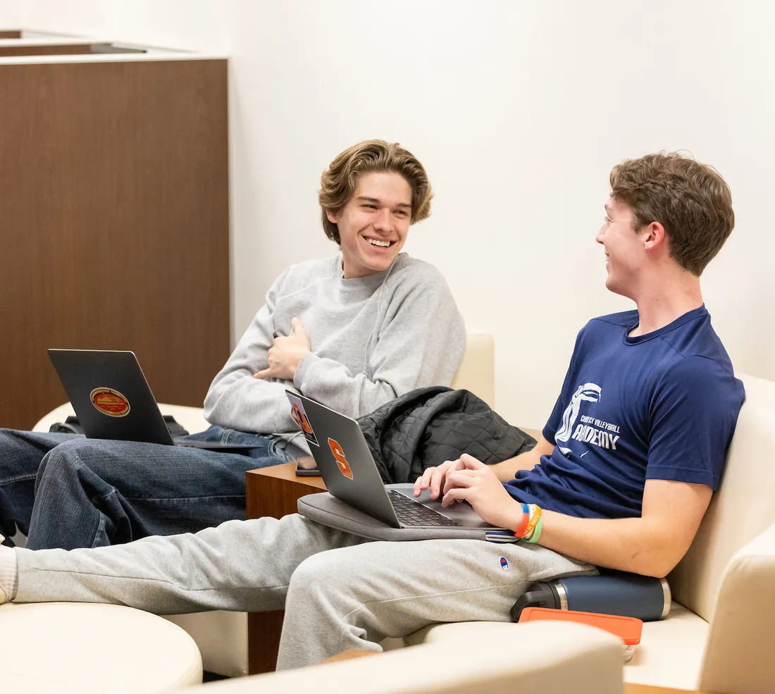 Two students sitting with their laptops on their laps.