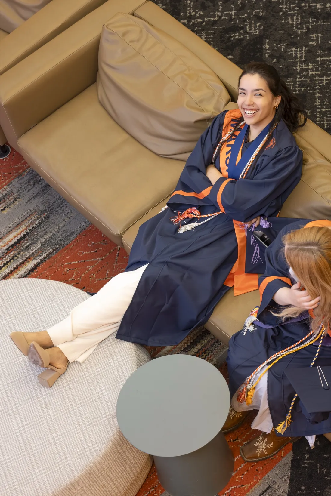 Ailed Torres Espinosa '26 dressed in her graduation regalia sitting on a couch and smiling in the Barnes Center at The Arch.