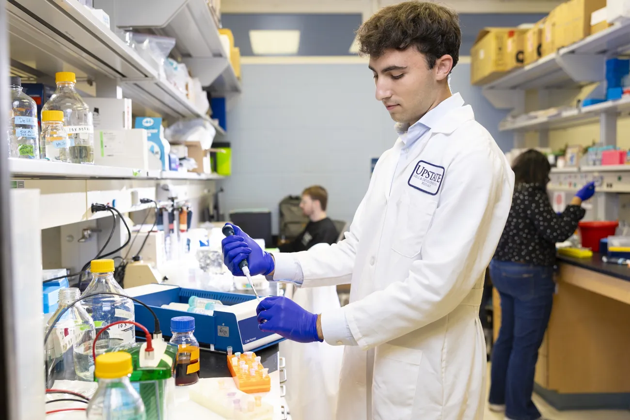 Beckam Polis ’28 using a pipette in a science lab, wearing a lab coat and latex gloves.
