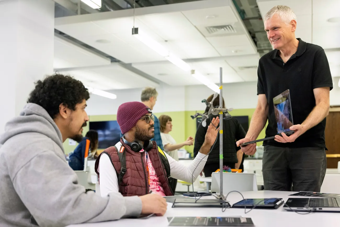 Professor and Don Carr speaking with InclusiveU student Chase Coleman and his caregiver, while holding a laptop.