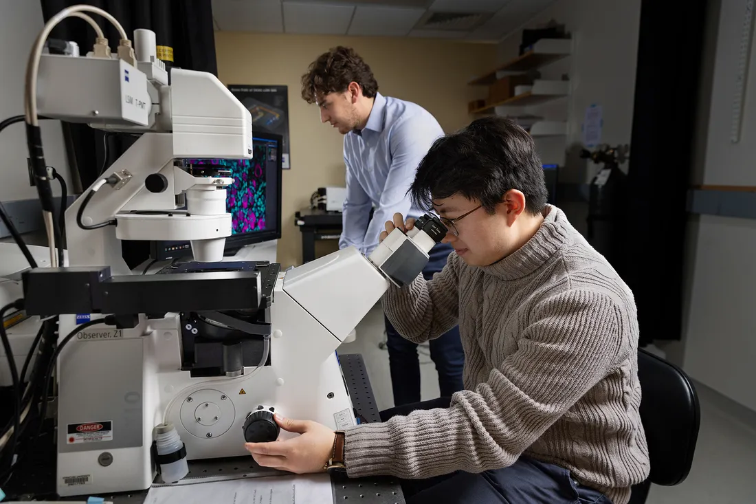 Male student looking through microscope lens.