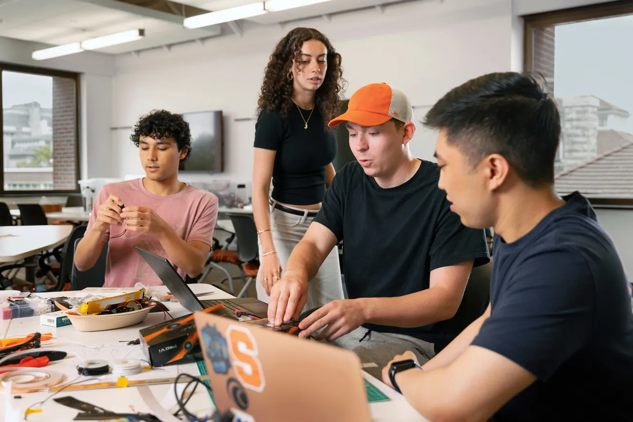 Four students working on computers and using tools.