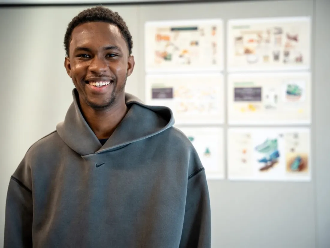 Abdulai Jibril Barrie '26 standing and smiling in front of images of his footwear designs.