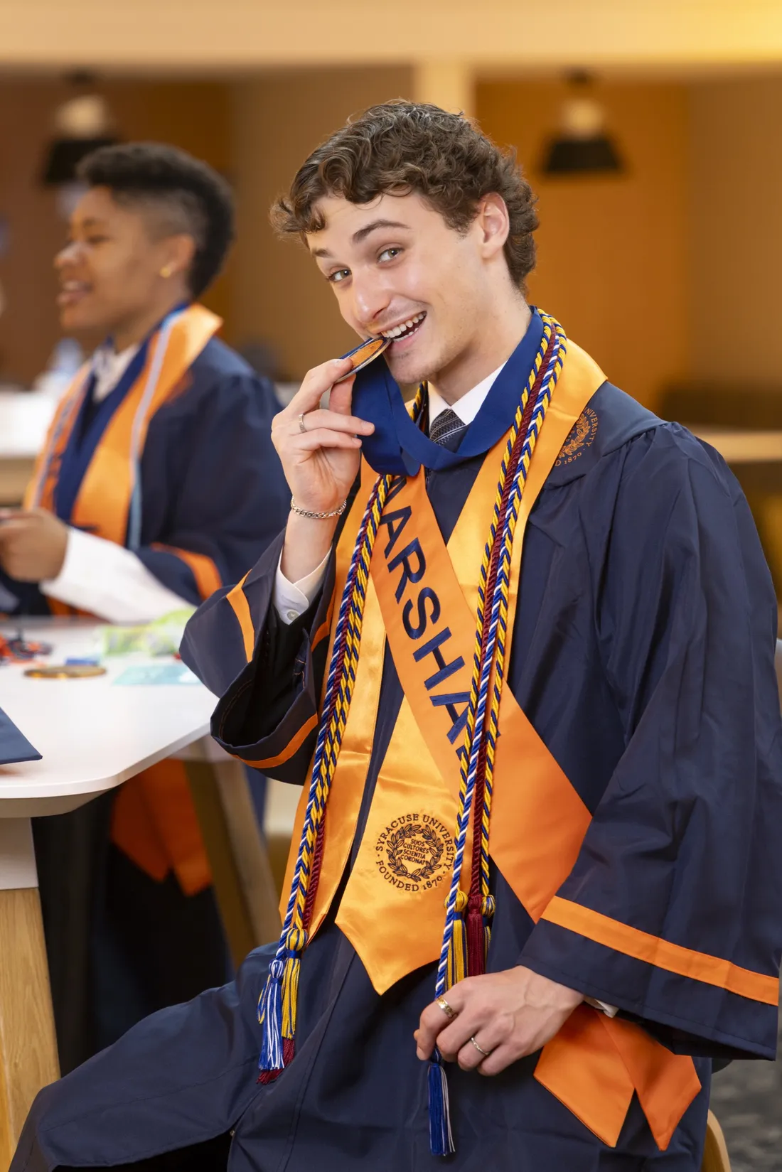 Steven Labovitch '26 dressed in graduation regalia biting his commencement medal in a celebratory manner.