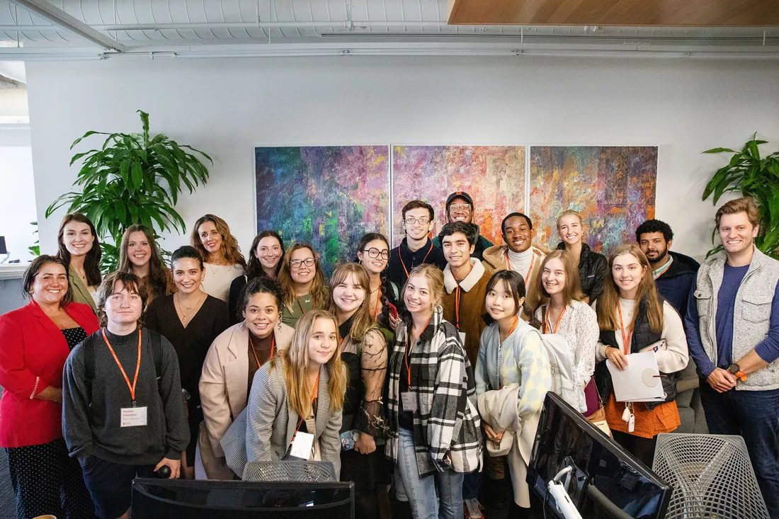 Group photo of students, posed in front of pieces of art hung on the wall.