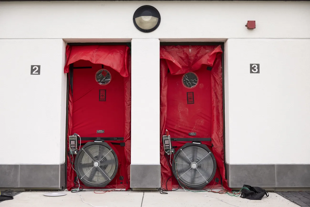 Two doors to the retrofitted apartments on South Campus, with fans and air leakage tracking technology attached.