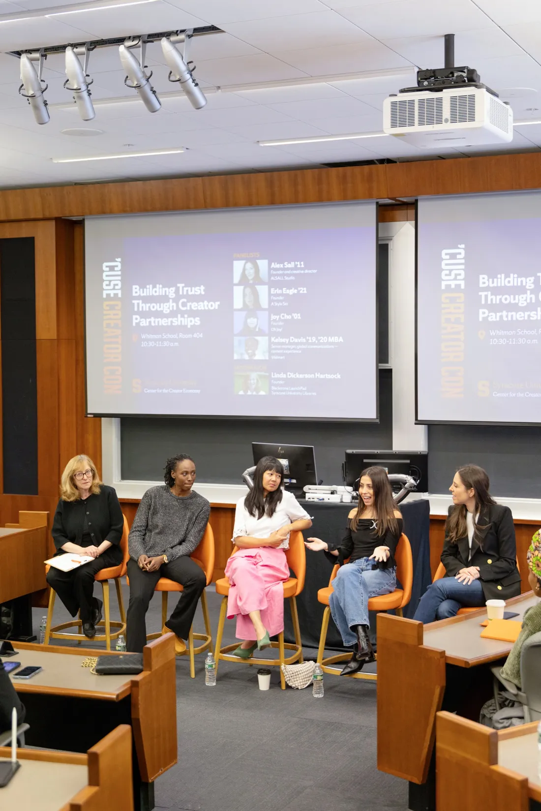 Five women sitting at the front of a lecture hall speaking for a panel.