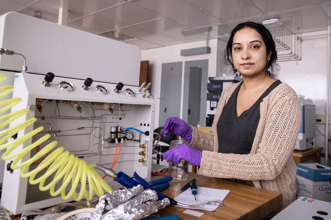 Woman in lab wearing PPE studying at a machine.
