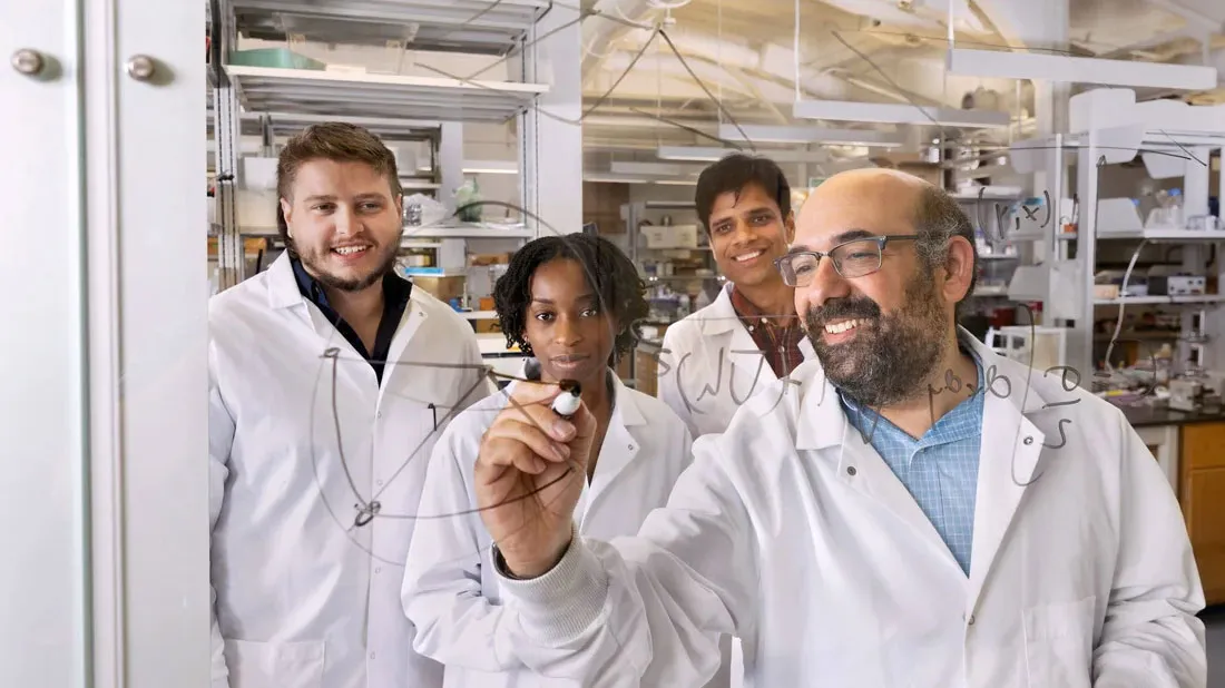 Four researchers writing a formula on glass board.