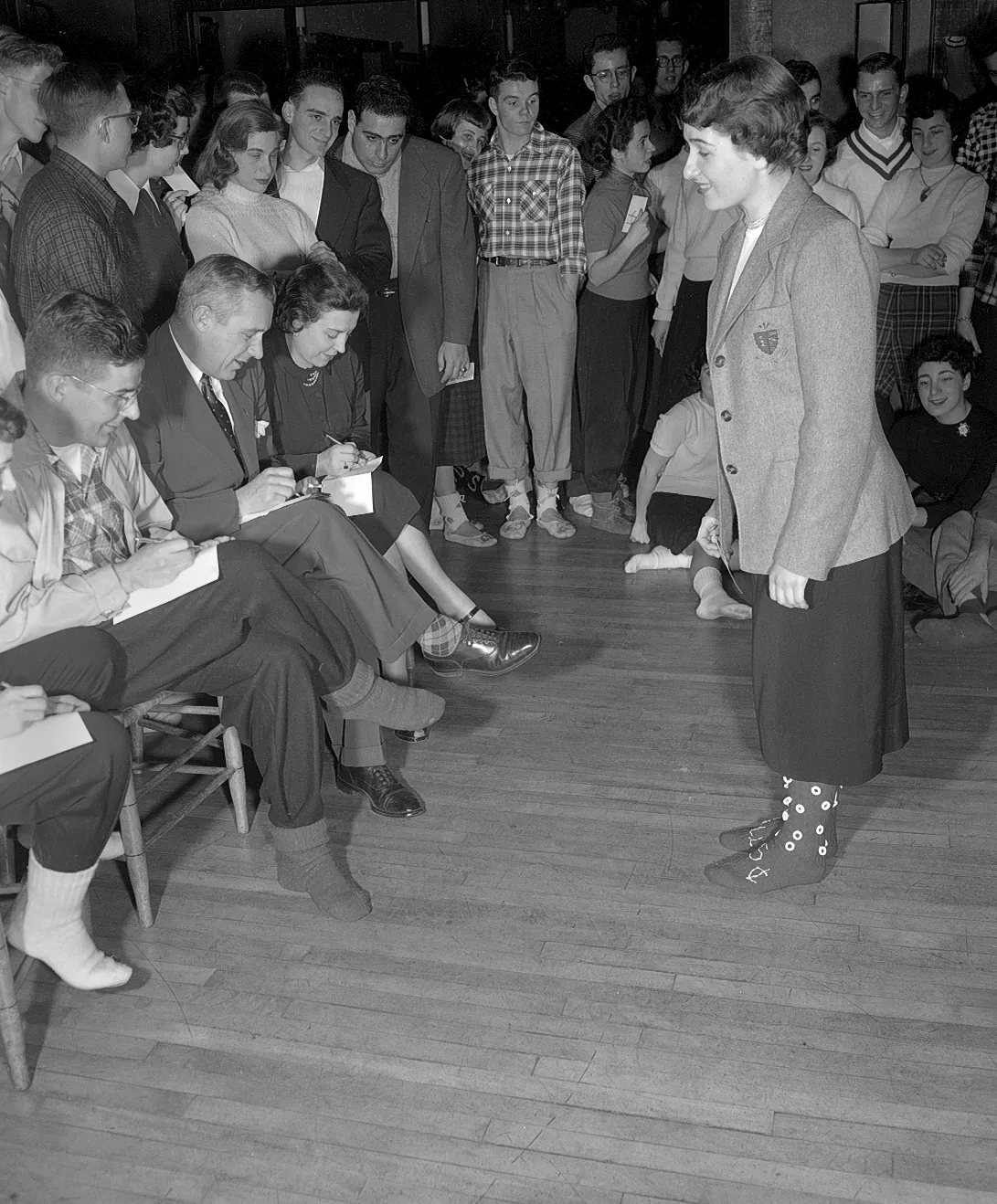 Group of people standing and sitting, looking at the socks of a standing person.