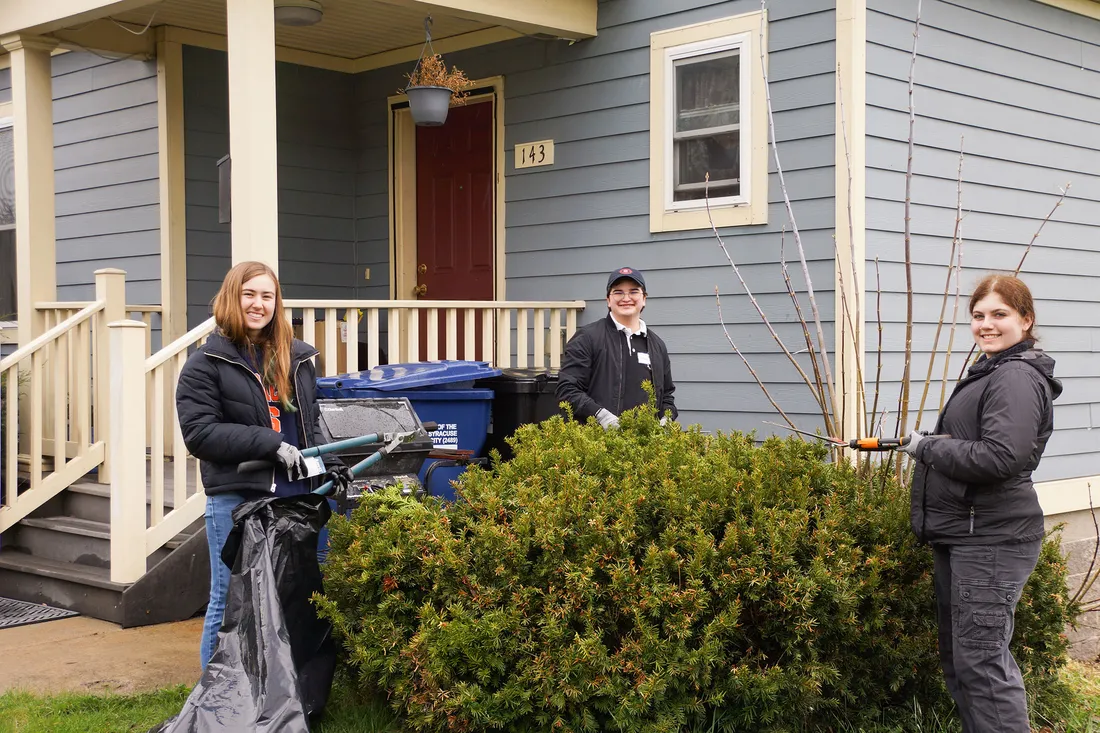 People outside of a house doing yard work for Orange Seeds.