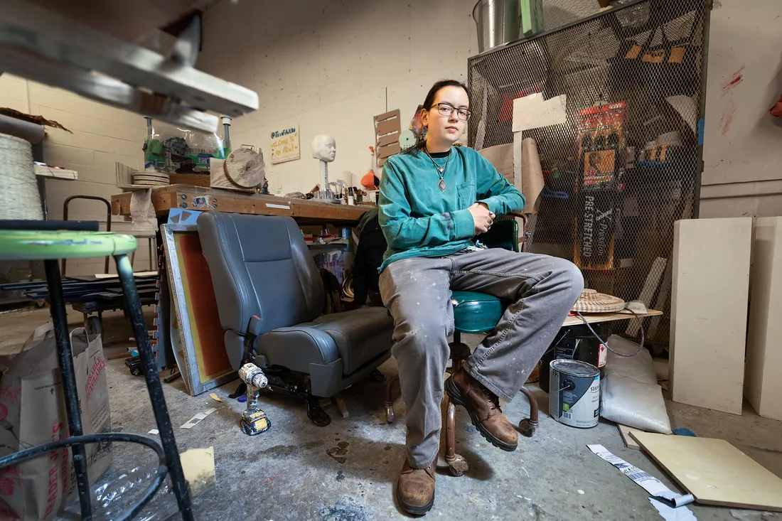 Student sitting staring at camera surrounded by artwork in an art studio.