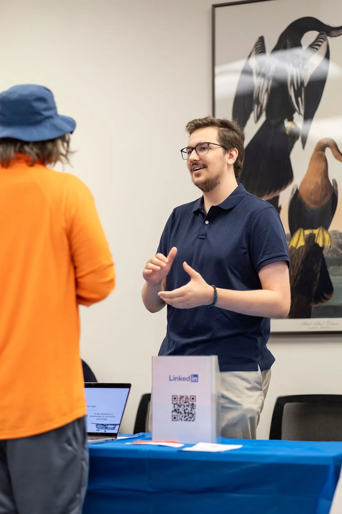 A student standing at a table at a Launchpad Alumni Mixer talking to another person.