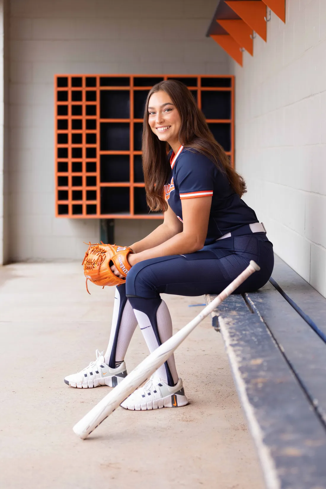 Olivia Pess ’24 smiling and sitting with glove and bat.