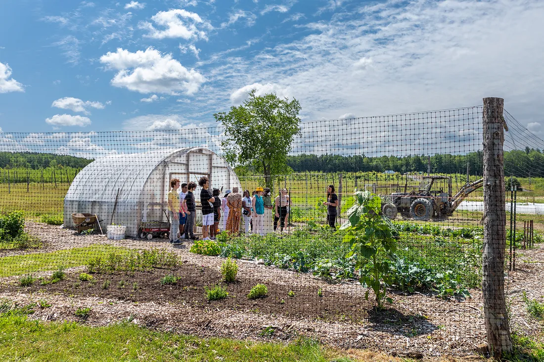 Landscape of Charles' garden beds and greenhouse with visiting students paying close attention to her lecture.