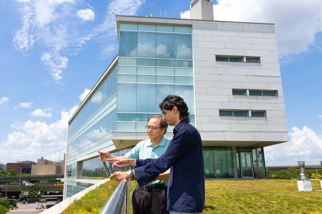 Emanuel Boutros '27 and Professor Jianshun Zhang looking at a laptop on top of the Center of Excellence building.