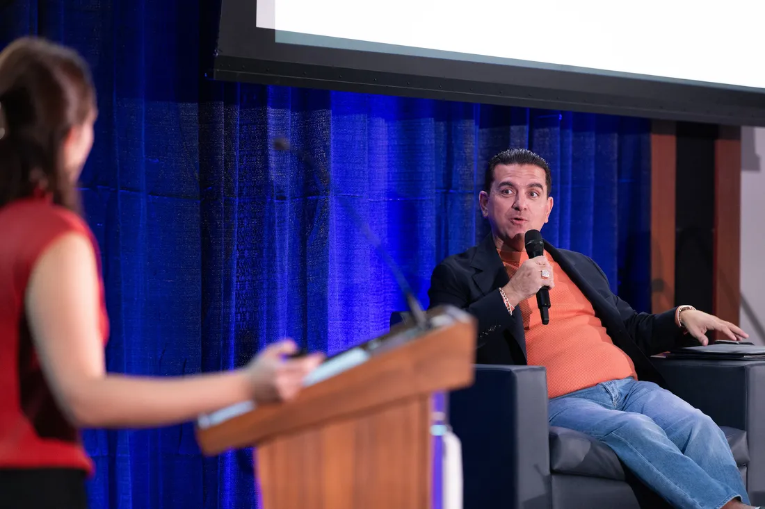 Person speaking into a microphone on the stage at Orange Tank.