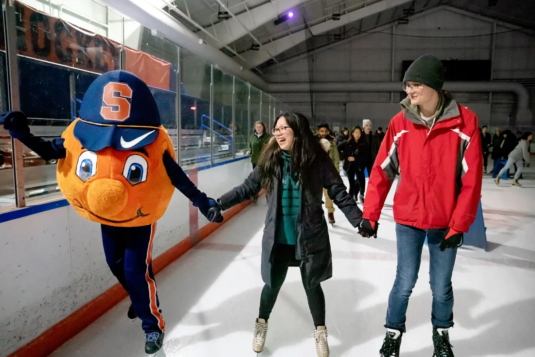 Two people and Otto the mascot holding hands and ice skating.