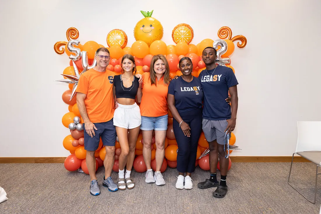 Parents and their students pose together in front of balloon background.