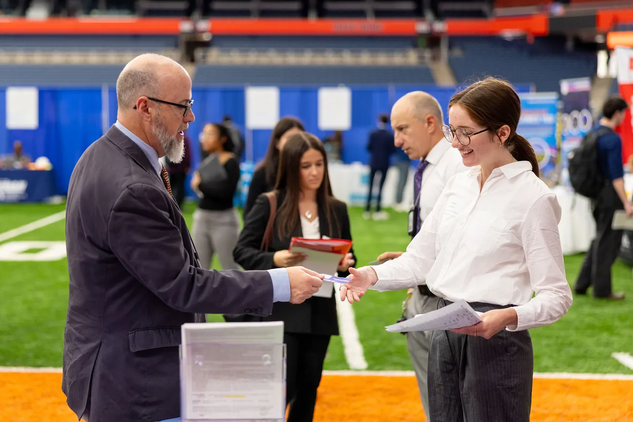 Student handing a person a resume at a career fair.
