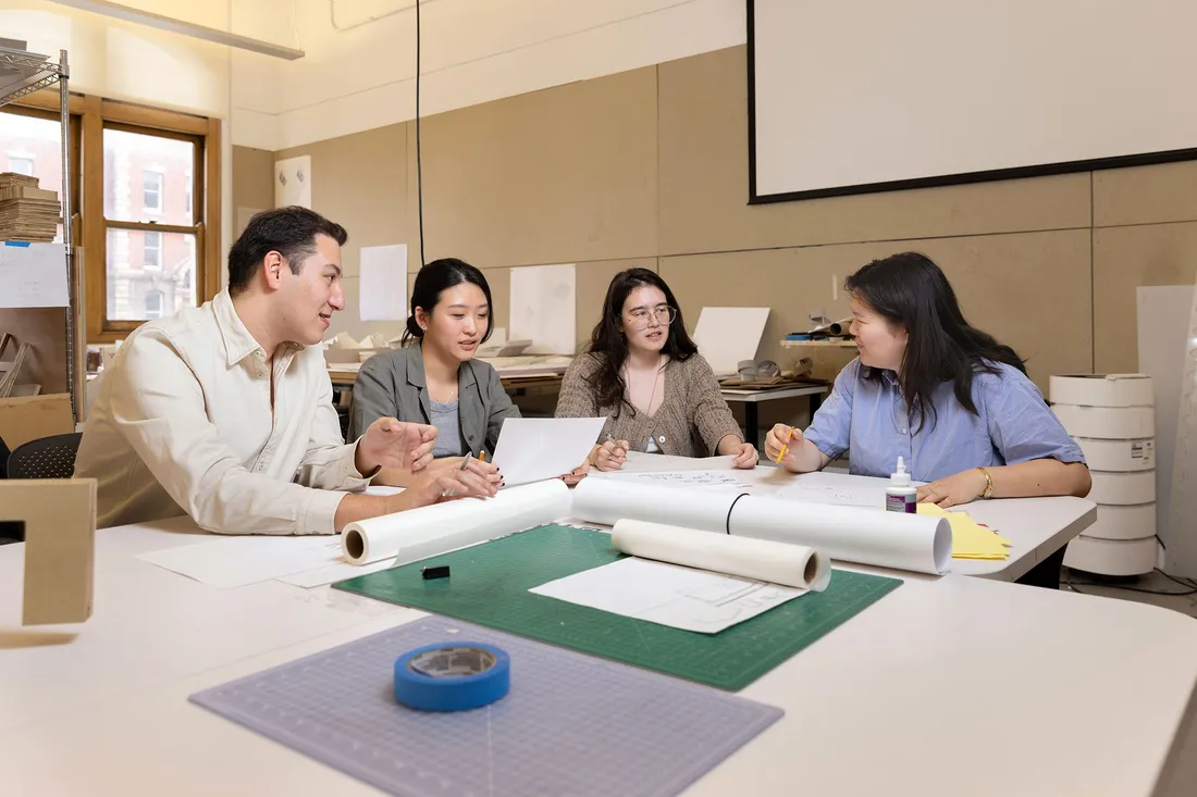 A group of students in the School of Arcihtecture talking at a table.