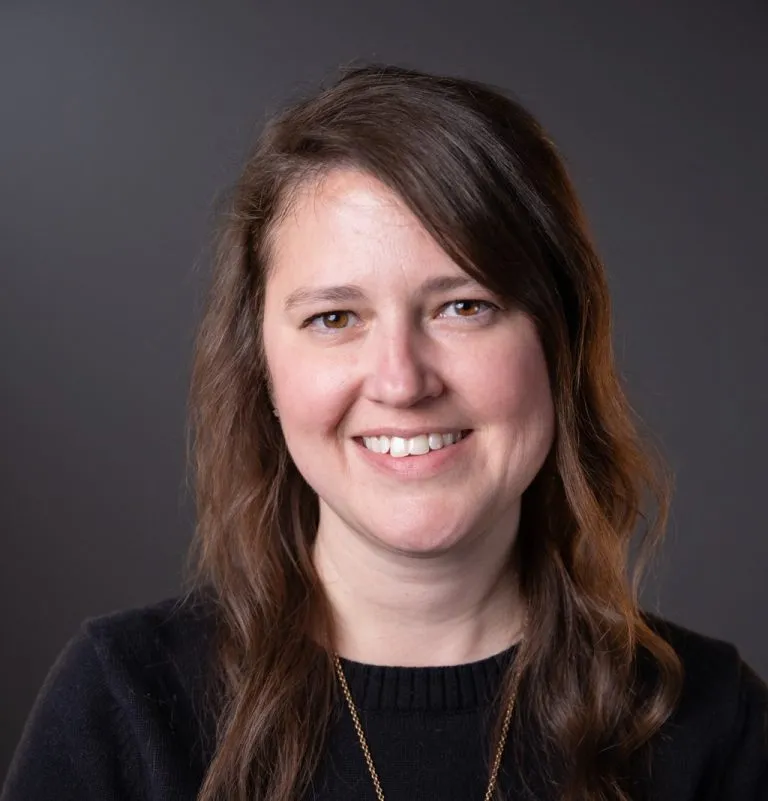Beck Straub smiling in front of a grey background.