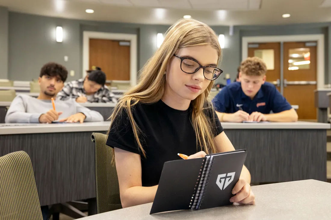 Person sitting in a classroom taking notes in a notebook.