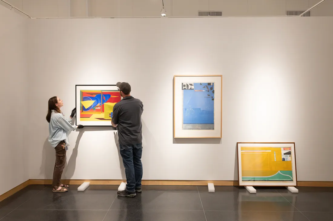People work to hang photo on a wall in a museum.