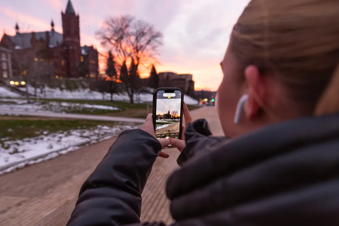 A person taking a picture of the sunset on campus.