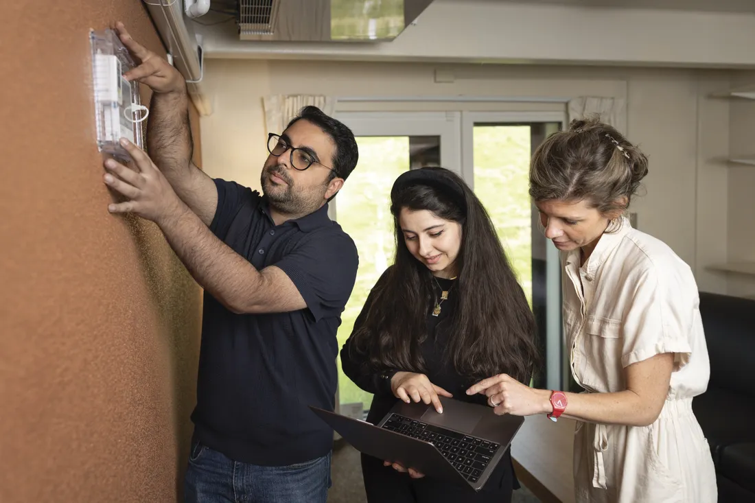 Three Syracuse University researchers checking a smart thermostat inside one of the retrofitted South Campus apartments.