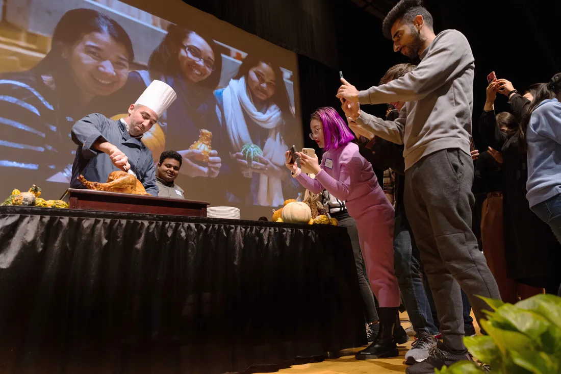 Wide shot of international students photographing as a turkey is being carved by a chef at the International Thanksgiving Dinner in the Schine Student Center.
