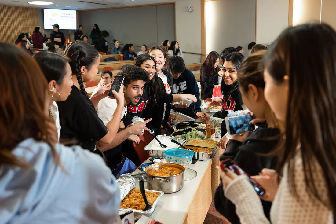 Students gather around food table exploring options on a buffet of food.