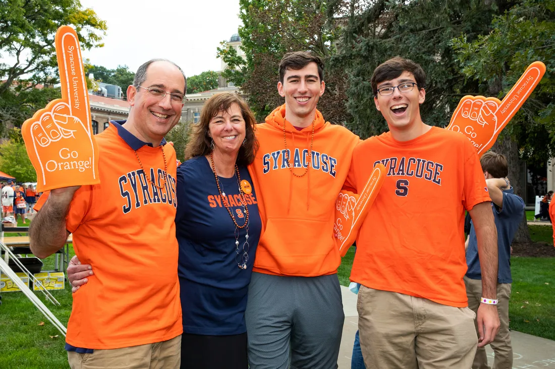 Syracuse University family wearing Orange apparel and holding Go Orange foam fingers on campus