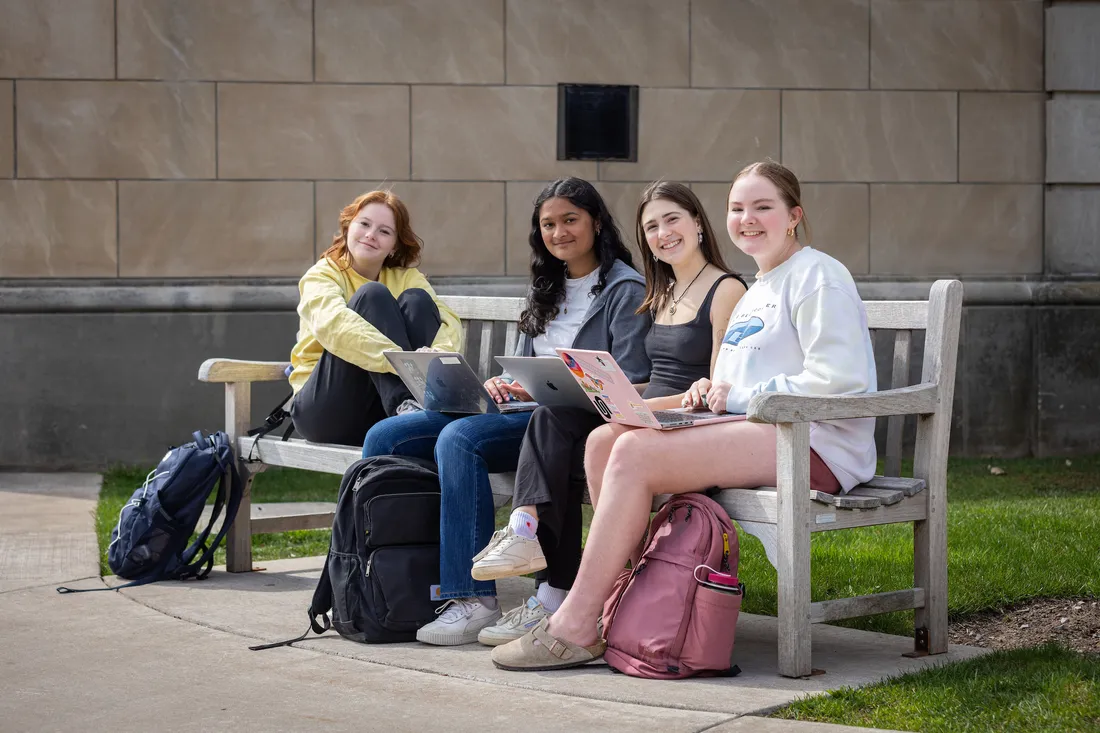 Four people smiling and sitting on a bench.