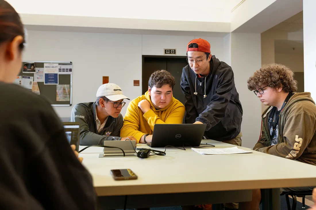 Students and mentors gather around a laptop reviewing software.
