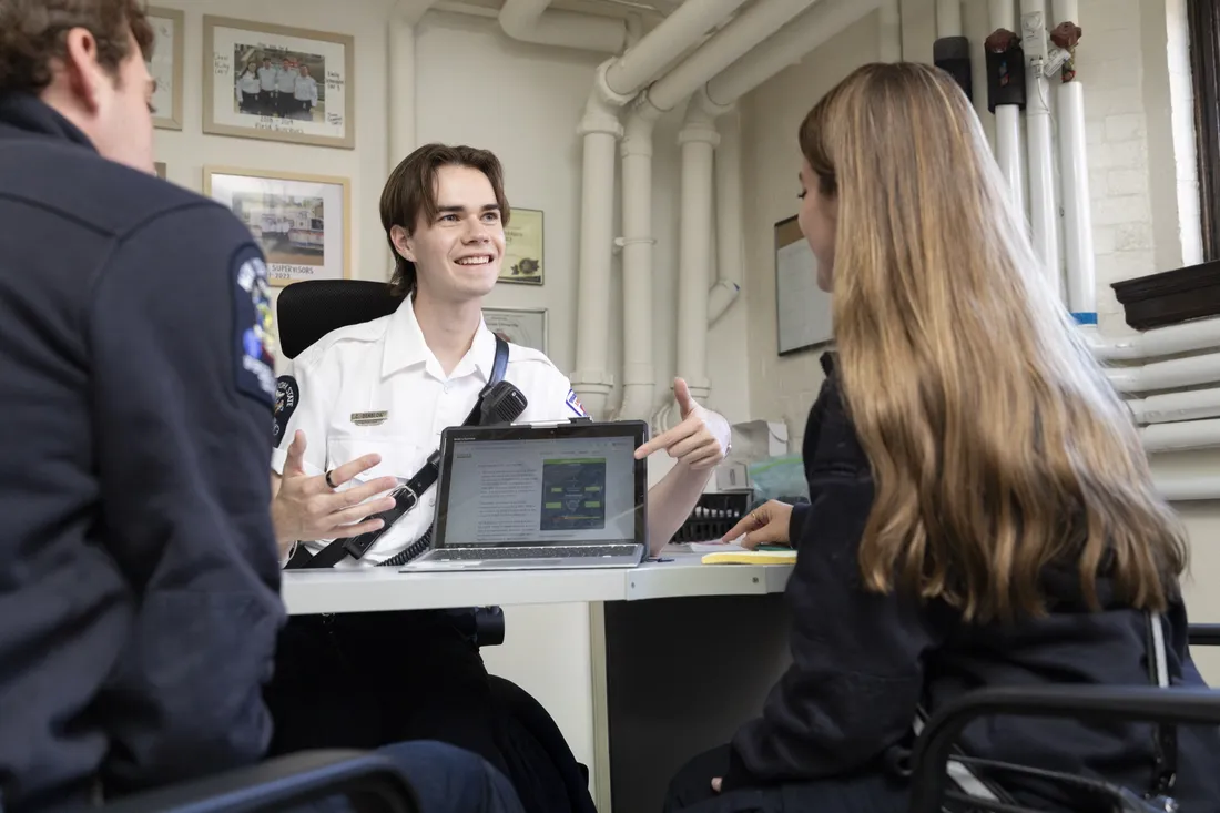 Person sitting at desk speaking with two other people.