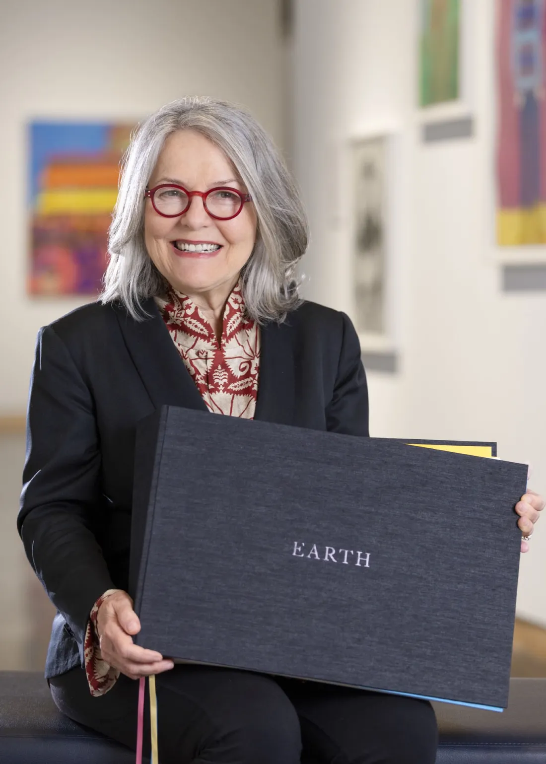 Alumna Diana Wege holding a large book with the word Earth printed on it.
