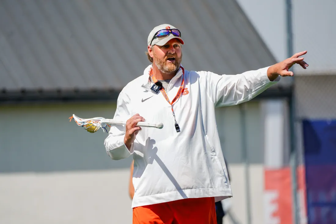 Syracuse University womens lacrosse coach, Regy Thorpe, standing and holding lacrosse stick.