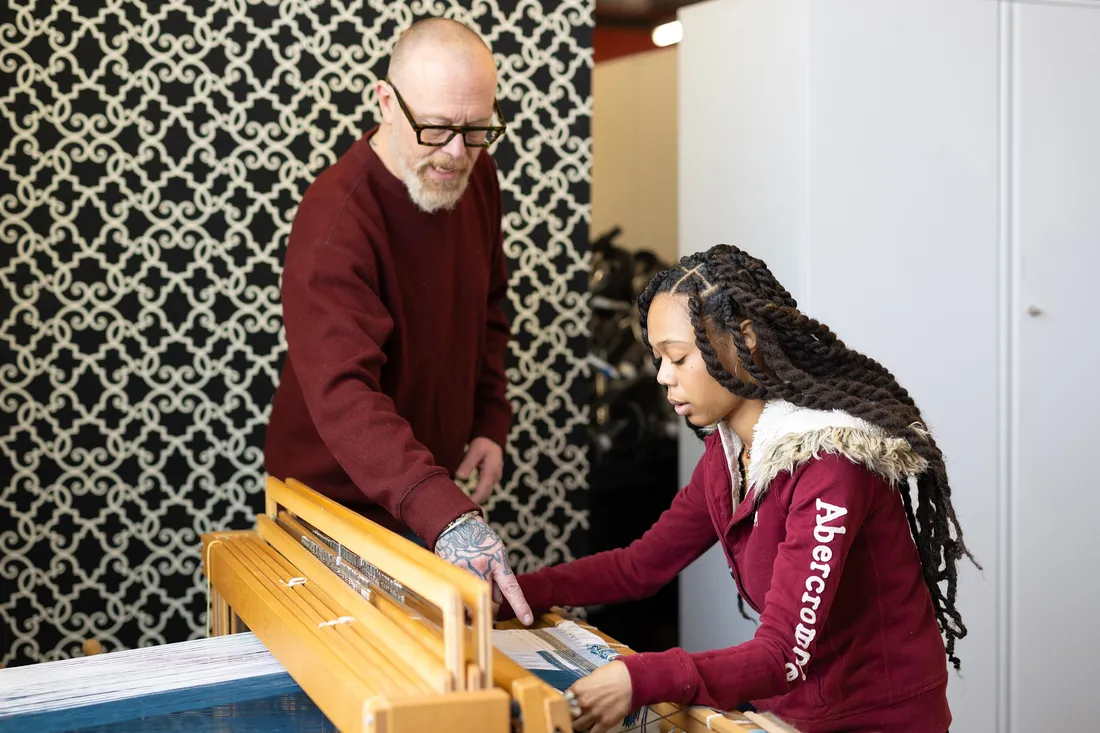 Professor Todd Conover '95 mentoring a student using a loom to weave fibers.