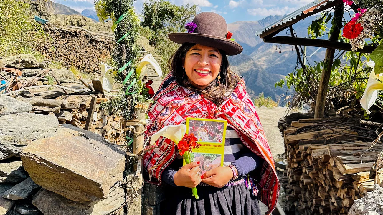 Person in traditional Peruivan clothing holding a book outside.
