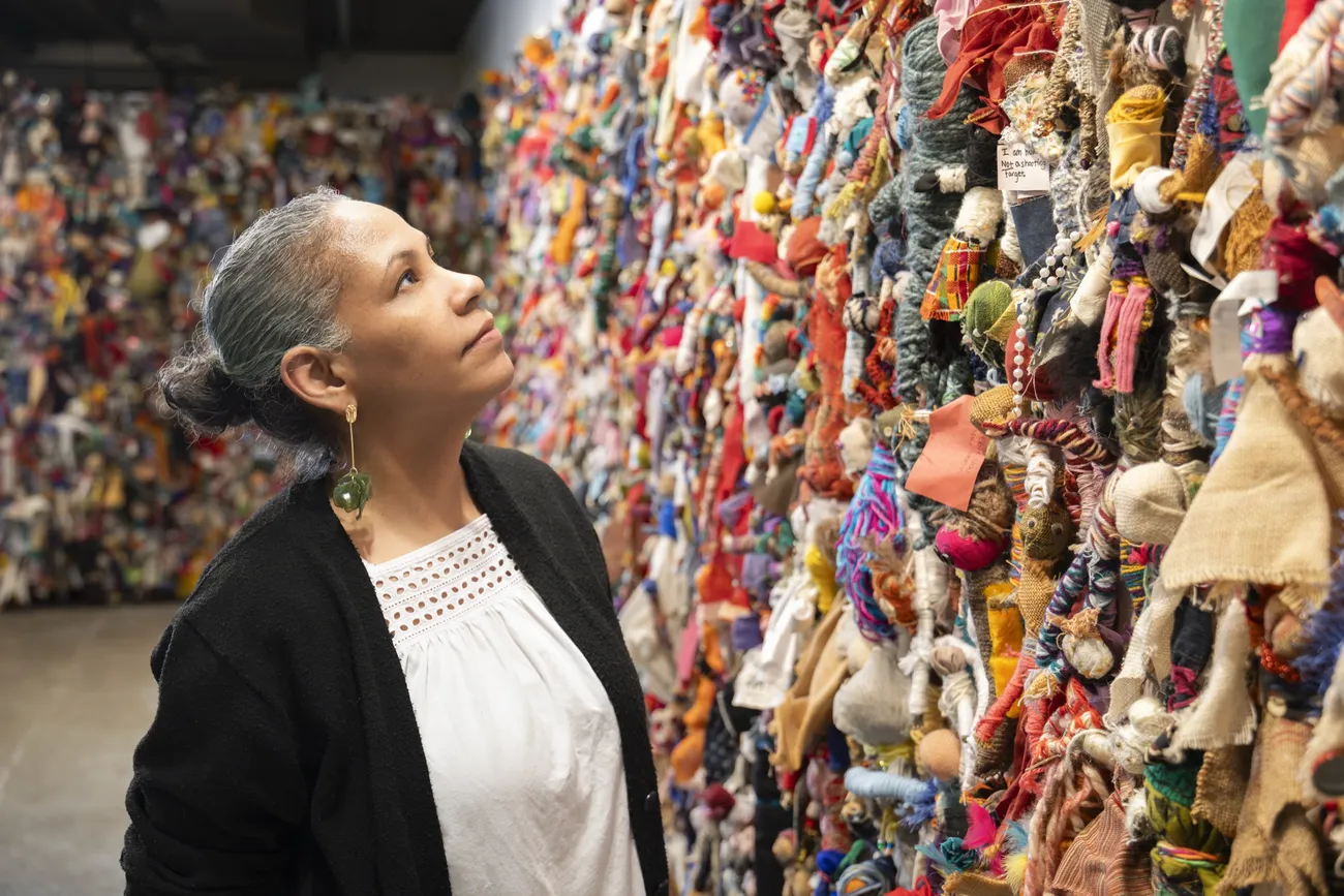 Professor Rochele Royster looks up at an art piece of cloth dolls.
